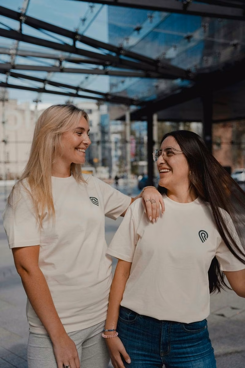 Two colleagues in cream Smaller Earth T-shirts laughing together on a city street